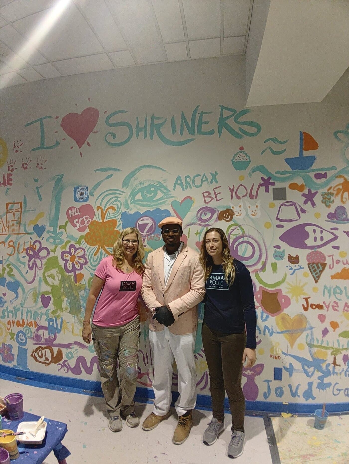 Three people in front of a wall covered edge to edge in community drawings and handprints.
