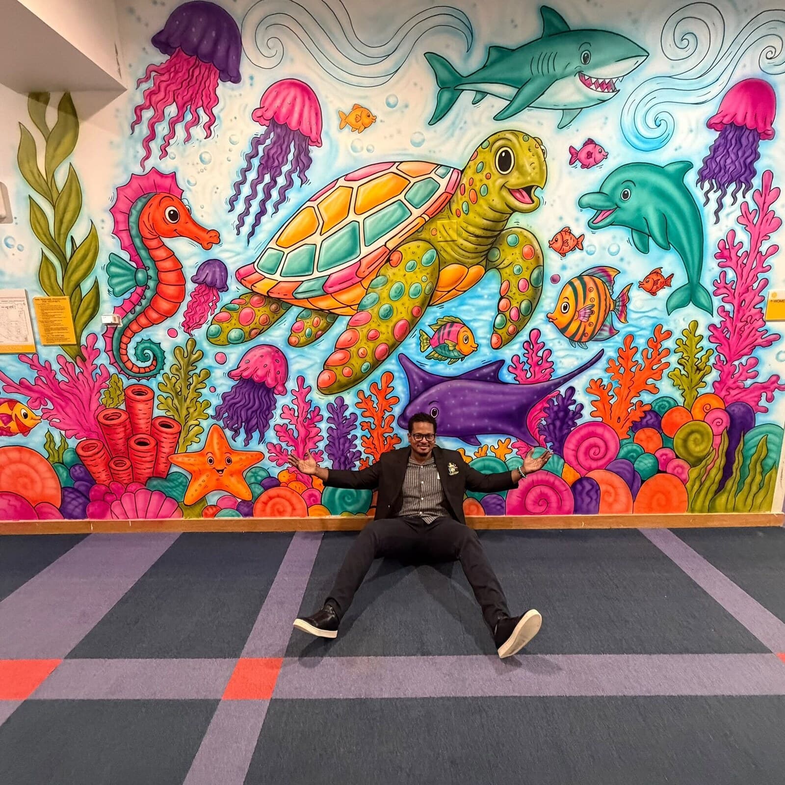 Jamaal Rolle with arms thrown wide in front of the finished coral reef mural.
